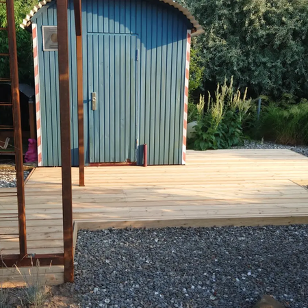 Eine blaue Gartenhütte auf einer Holzterrasse