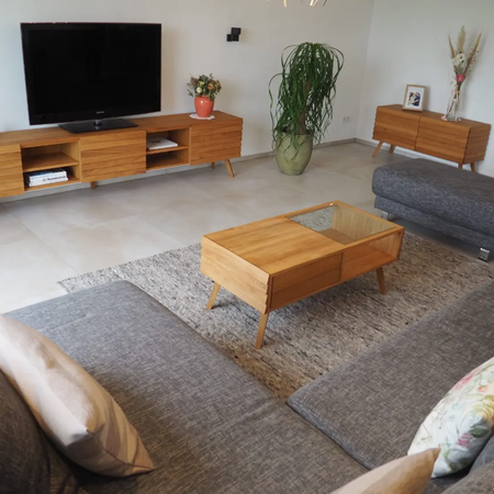 Blick in ein Wohnzimmer mit TV-Board, einem Sideboard und einem Wohnzimmertisch, der zwischen dem Sofa und einem Hocker steht